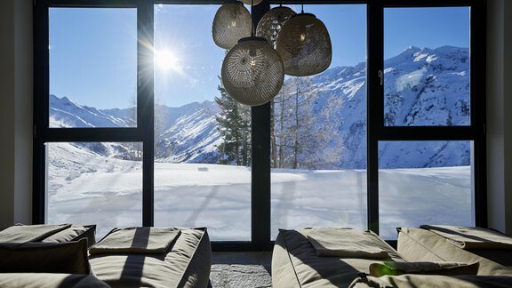 A cozy room with two loungers and large windows. Outside, the sun shines over snow-covered mountains. - Alpenhotel Laurin - Hochgurgl