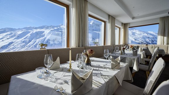 An elegant restaurant with beautifully set tables. The large windows offer a breathtaking view of the snow-covered mountains. - Alpenhotel Laurin - Hochgurgl