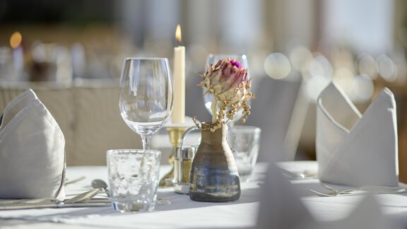 An elegantly set table with glasses, cutlery, and a small floral arrangement. A burning candle creates a cozy atmosphere. - Alpenhotel Laurin - Hochgurgl