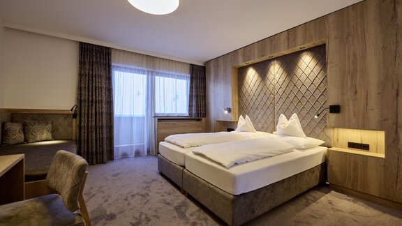 A modern bedroom with two beds and warm wooden tones. Large windows provide plenty of daylight and a cozy atmosphere. - Alpenhotel Laurin - Hochgurgl