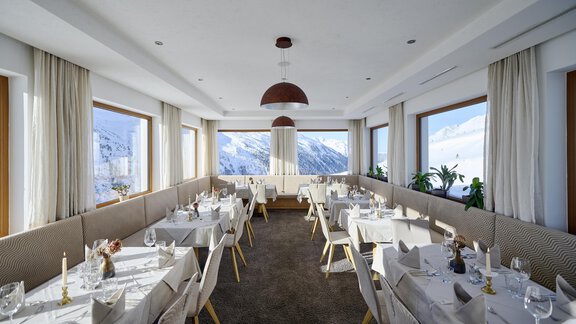 An elegant restaurant with white tables and chairs. Large windows offer a view of the snow-covered mountains. - Alpenhotel Laurin - Hochgurgl