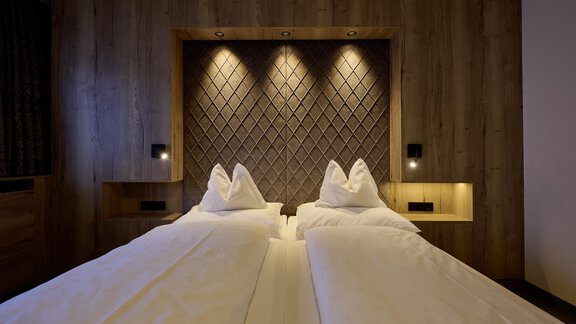 A modern bedroom with two single beds. The walls are made of wood, and the lighting creates a cozy atmosphere. - Alpenhotel Laurin - Hochgurgl