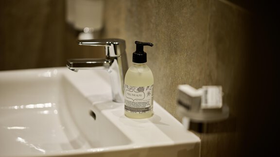 A modern sink with an elegant faucet. A bottle of hand soap is next to the sink on the shelf. - Alpenhotel Laurin - Hochgurgl