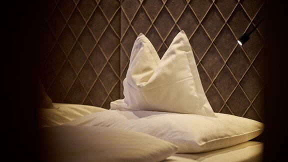 A cozy bed with white pillows in an elegant room. The walls are designed with a modern, simple pattern. - Alpenhotel Laurin - Hochgurgl