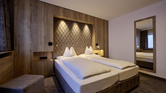 A modern bedroom with two single beds and wood paneling. The room is bright and cozy, with a large mirrored surface. - Alpenhotel Laurin - Hochgurgl