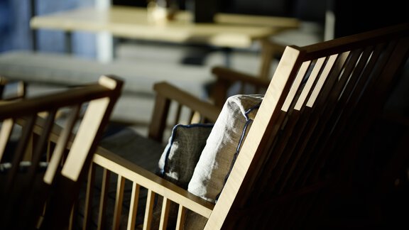 A cozy wooden chair with a cushion is in the foreground. In the background, a table is visible, conveying a relaxed atmosphere. - Alpenhotel Laurin - Hochgurgl