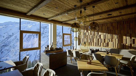 A modern restaurant with wooden decor and large windows. The view shows snow-covered mountains in the background. - Alpenhotel Laurin - Hochgurgl