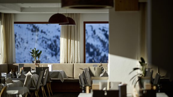 A stylish restaurant with modern furniture and large windows. Through the windows, a snow-covered landscape is visible. - Alpenhotel Laurin - Hochgurgl