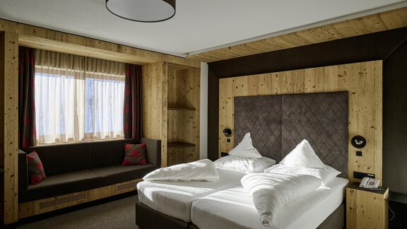 A cozy hotel room with two single beds and modern wood design. Large window with a view of the outside world and a comfortable sitting area. - Alpenhotel Laurin - Hochgurgl