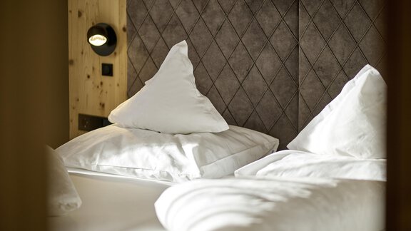 A cozy bedroom with two beds and soft, white pillows. The walls are made of wood and feature a modern design. - Alpenhotel Laurin - Hochgurgl