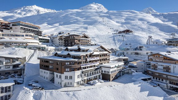 A snow-covered mountain landscape with several chalet houses. The radiant blue sky accentuates the wintry atmosphere. - Hotel Angerer Alm - Hochgurgl