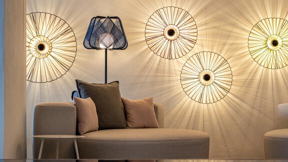 An elegant living room with a beige sofa and a lamp. Decorative, round lamps are installed on the wall, emitting warm light. - Hotel Angerer Alm - Hochgurgl