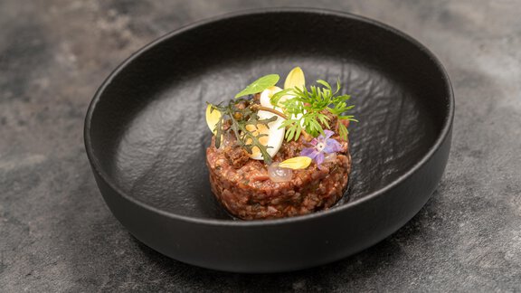 A beautifully arranged dish in a black bowl. The food consists of tender meat, garnished with fresh herbs and edible flowers. - Hotel Angerer Alm - Hochgurgl