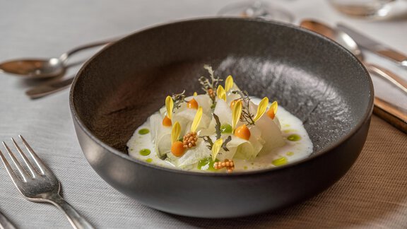 An elegant bowl with a fine dish, garnished with colorful flowers and herbs. The plate is artfully arranged and highlights the fresh ingredients. - Hotel Angerer Alm - Hochgurgl
