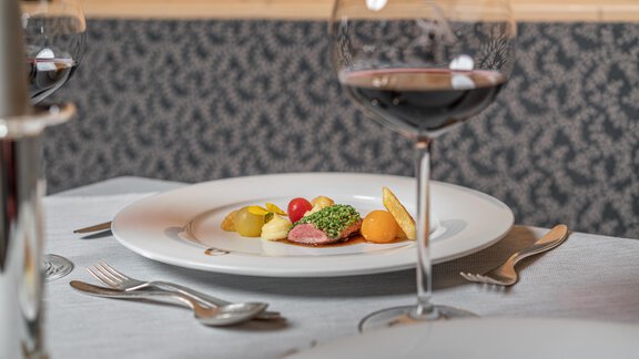 An elegant meal on a table with cutlery. In the foreground, a plate with various types of vegetables and a glass of red wine. - Hotel Angerer Alm - Hochgurgl