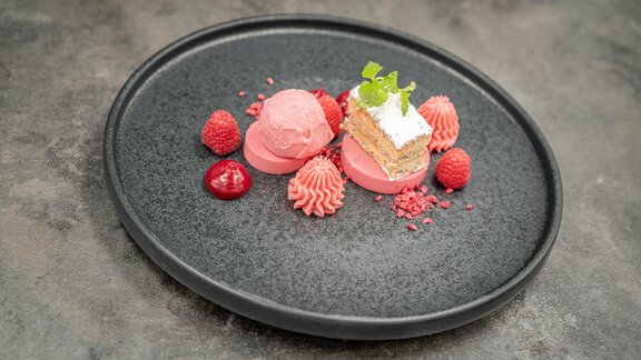 A modern plate with pink ice cream, berries, and a small cake. The decoration includes fresh mint and artfully shaped cream. - Hotel Angerer Alm - Hochgurgl