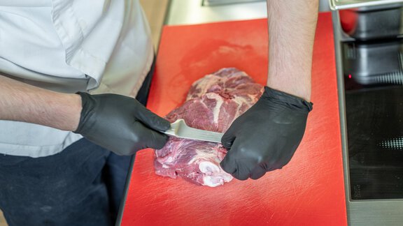 A chef is slicing meat on a red cutting board. The chef is wearing black gloves. - Hotel Angerer Alm - Hochgurgl