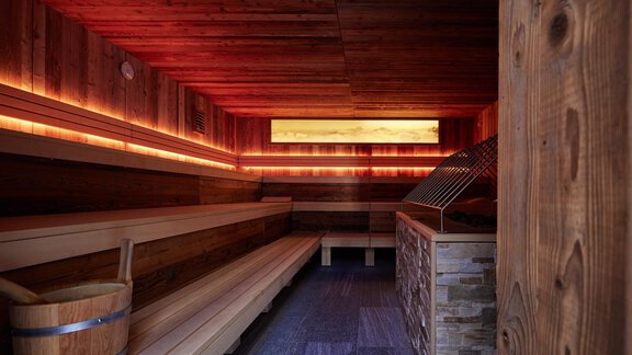 Eine moderne Sauna mit Holzbank und stimmungsvollem Licht. Auf der linken Seite steht ein Holzfass. - TOP Hotel Hochgurgl - Hochgurgl