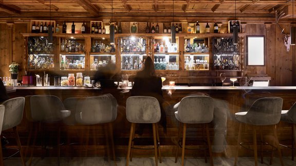 Eine gemütliche Bar mit Holzinterieur und einer großen Auswahl an Getränken. Menschen sitzen an der Bartheke und genießen ihre Drinks. - TOP Hotel Hochgurgl - Hochgurgl