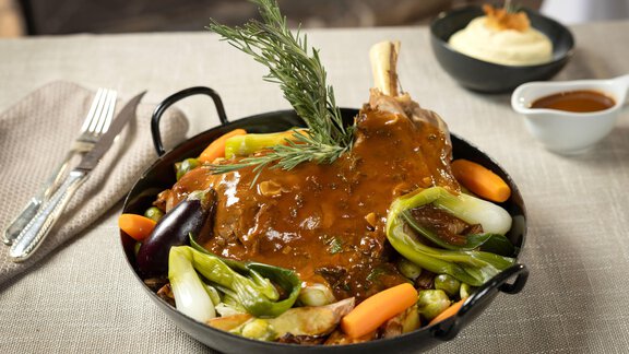 Ein köstliches Gericht mit einem großen Stück Fleisch, umgeben von buntem Gemüse. Dazu gibt es eine kleine Schüssel mit Sauce und ein Beilagen-Gericht. - TOP Hotel Hochgurgl - Hochgurgl