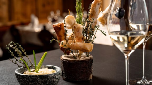 Ein kunstvoll angerichteter Teller mit verschiedenen Snacks und Kräutern auf einem Tisch. Im Hintergrund sind Gläser und eine gemütliche Atmosphäre zu sehen. - TOP Hotel Hochgurgl - Hochgurgl