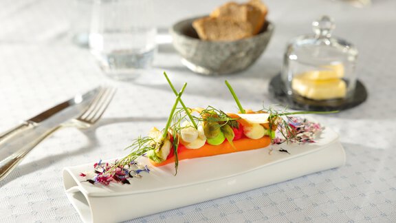 Ein kunstvoll angerichteter Teller mit einer bunten Vorspeise und frischen Kräutern. Im Hintergrund sind Wasser, Brot und Butter zu sehen. - TOP Hotel Hochgurgl - Hochgurgl