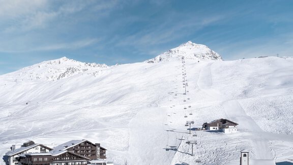 Ein winterliches Bergpanorama mit schneebedeckten Hängen und einem Skilift. Im Vordergrund sieht man ein gemütliches Hotel. - TOP Hotel Hochgurgl - Hochgurgl