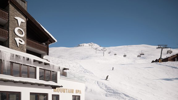 Ein schneebedeckter Hang mit Skiliften und einigen Skifahrern. Im Vordergrund steht ein modernes Gebäude mit dem Schriftzug „TOP“. - TOP Hotel Hochgurgl - Hochgurgl