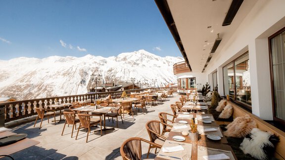 Eine gemütliche Außenterrasse eines Restaurants mit Blick auf schneebedeckte Berge. Die Tische sind schön eingedeckt und bieten einen einladenden Platz zum Essen. - TOP Hotel Hochgurgl - Hochgurgl