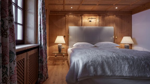 Ein gemütliches Schlafzimmer mit Holzwänden und einem großen Bett. Die Beleuchtung sorgt für eine warme und einladende Atmosphäre. - TOP Hotel Hochgurgl - Hochgurgl