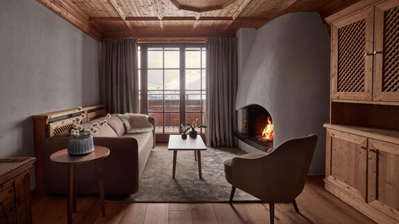 Ein gemütliches Wohnzimmer mit Holzverkleidung und einer Kaminfeuerstelle. Große Fenster bieten eine Aussicht auf die Berge und der Raum ist stilvoll eingerichtet. - TOP Hotel Hochgurgl - Hochgurgl