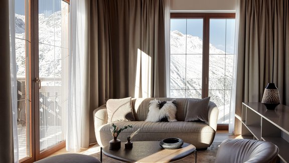 Ein modernes Wohnzimmer mit großen Fenstern und Blick auf schneebedeckte Berge. Es ist gemütlich eingerichtet mit einem hellen Sofa und stilvollen Möbeln. - TOP Hotel Hochgurgl - Hochgurgl