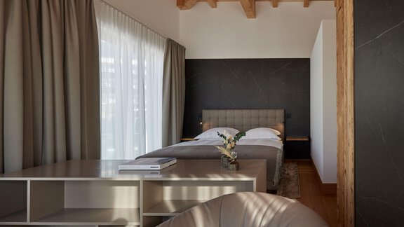 Ein modernes Schlafzimmer mit einem gemütlichen Bett und großen Fenstern. Der Raum ist hell und minimalistisch eingerichtet, mit Holz- und Stoffelementen. - TOP Hotel Hochgurgl - Hochgurgl