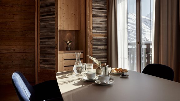 Ein elegantes Zimmer mit einem großen Tisch und einer Kaffeetasse. Durch die Fenster ist der Blick auf die Berge sichtbar, und es gibt eine gemütliche Atmosphäre. - TOP Hotel Hochgurgl - Hochgurgl