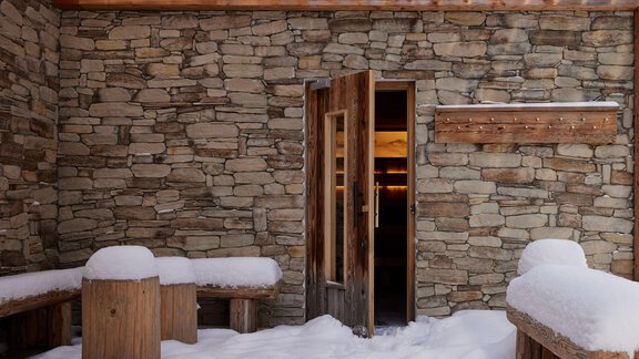 Ein rustikaler Raum mit Steinwänden und einer offenen Tür. Draußen liegt Schnee und es gibt hölzerne Bänke. - TOP Hotel Hochgurgl - Hochgurgl