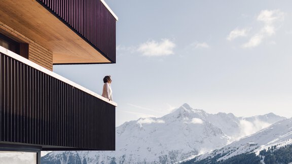 A woman stands on the balcony of a modern building. In the background, snow-covered mountains and a clear sky are visible. - 4 * Superior Hotel Schöne Aussicht - Hochsölden