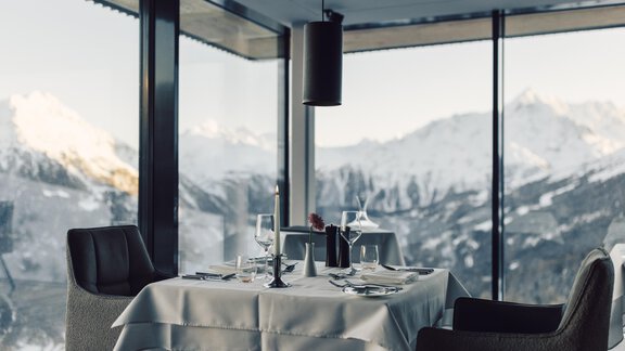 An elegant restaurant with a table and chairs that offers a stunning view of snow-capped mountains. The large windows let in plenty of daylight. - 4 * Superior Hotel Schöne Aussicht - Hochsölden