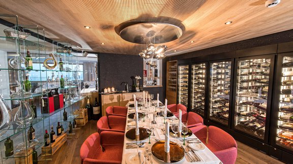 An elegant restaurant with stylish red chairs and a festively laid table. In the background, wine coolers and modern lighting can be seen. - 4 * Superior Hotel Schöne Aussicht - Hochsölden