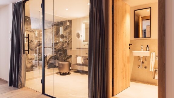 A modern bathroom with a large glass door and elegant wood details. There is a shower and a freestanding sink in a tasteful design. - 4 * Superior Hotel Schöne Aussicht - Hochsölden