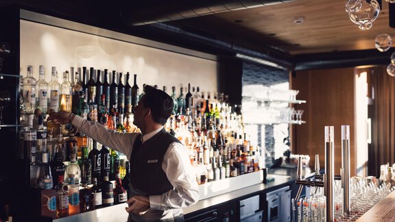 A bartender stands behind the bar and reaches for a bottle. The wall is decorated with a variety of drinks and spirits. - 4 * Superior Hotel Schöne Aussicht - Hochsölden