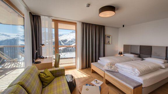 A modern hotel room with two beds and a cozy seating area. Large windows provide a view of the mountain landscape. - 4 * Superior Hotel Schöne Aussicht - Hochsölden