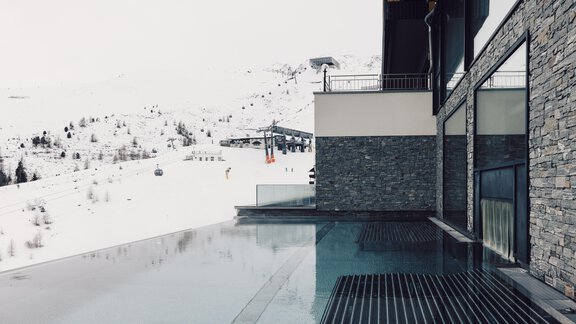 A modern building with an infinity pool overlooks snow-capped mountains. In the background, ski lifts are visible. - 4 * Superior Hotel Schöne Aussicht - Hochsölden