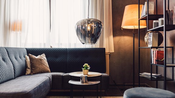 A modern living room with a gray sofa and a small table. A stylish lamp and bookshelf complement the decor. - 4 * Superior Hotel Schöne Aussicht - Hochsölden