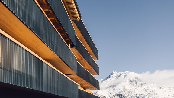 A modern building with a wood and metal facade in front of a snow-covered mountain landscape. The clear sky complements the stunning view. - 4 * Superior Hotel Schöne Aussicht - Hochsölden