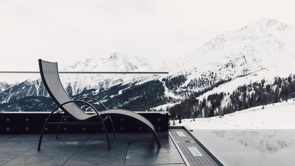 A stylish lounge chair stands on a terrace with a view of snow-covered mountains. The tranquil landscape exudes a relaxed atmosphere. - 4 * Superior Hotel Schöne Aussicht - Hochsölden