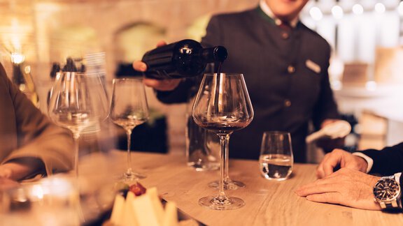A waiter is pouring wine into a large glass. On the table are glasses and a cheese platter. - 4 * Superior Hotel Schöne Aussicht - Hochsölden