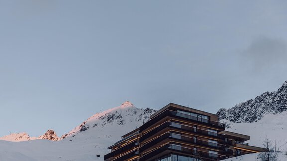 A modern hotel in the mountains, surrounded by snow-covered peaks. The sky is clear and the twilight casts a light pink hue over the mountains. - 4 * Superior Hotel Schöne Aussicht - Hochsölden