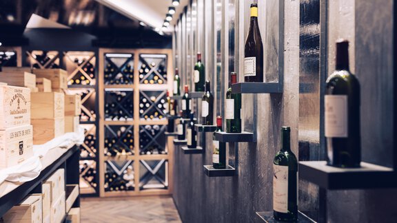 A modern wine cellar with shelves displaying various wine bottles. In the background, wooden boxes and additional bottles are visible. - 4 * Superior Hotel Schöne Aussicht - Hochsölden