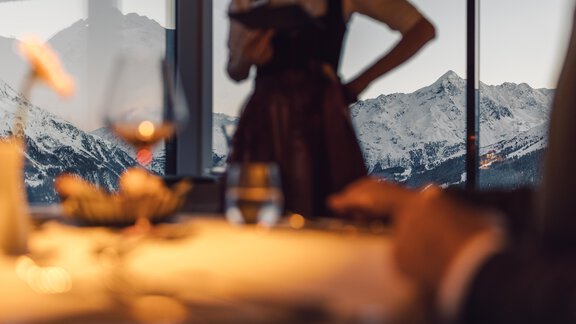 A beautiful view of snow-covered mountains through a large window. In the foreground, there is an elegant table decoration and a server in traditional attire. - 4 * Superior Hotel Schöne Aussicht - Hochsölden