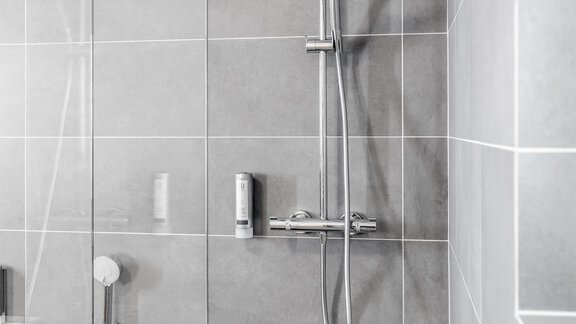 A modern shower with gray tiles and an elegant shower head. The bathtub is also visible and integrates harmoniously into the space. - Enzian Apartments - Hochsölden
